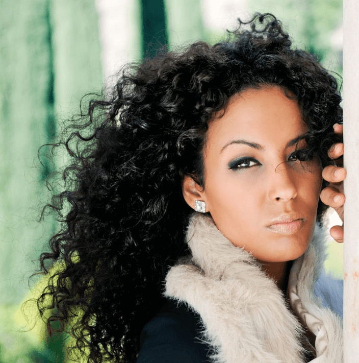 Woman with curly hair posing with dramatic makeup while wearing a stylish fur coat.