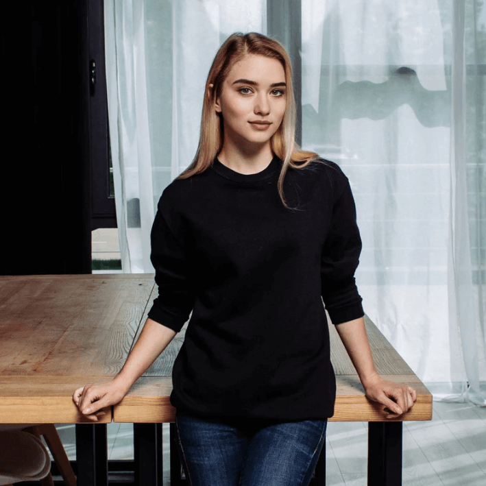 Ung kona í svörtu peysu stendur við viðarbord í björtu rými.